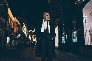 Bearded man in tuxedo walking in city at night in Christmas time