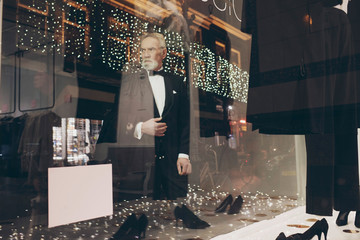 Senior man with beard in tuxedo window shopping at night in chri