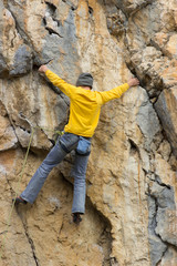 Young male climber hanging by a cliff.