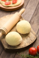 Small balls of yeast dough for pizza or flatbread with rolling pin on wooden board (Selective Focus, Focus on the front of the first dough ball)