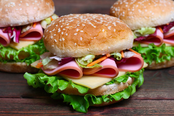 Burger sandwich with sausage, cheese and vegetables on a wooden background