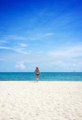 Young white fit woman in black bikini walking towards ocean