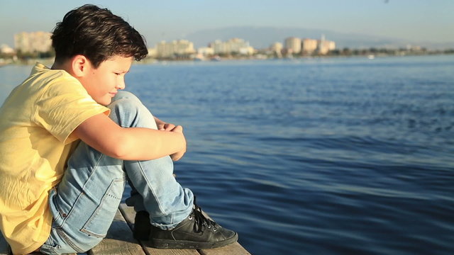 Lonely sad young boy on a wooden quay