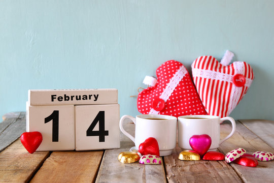 February 14th wooden vintage calendar with colorful heart shape chocolates next to couple cups on wooden table. selective focus