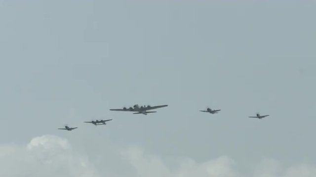 B-17 Flying Fortress leads four World War II fighter planes, approaching in formation, including a P-63 Kingcobra, a P-38 Lightning, and two P-51 Mustangs.  Recorded in 4K, ultra high definition. 