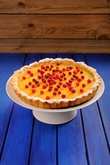 Yummy lemon pie with fresh cranberries on white stand on deep bl