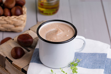 Chestnut soup in white enamel mug with roasted chestnuts 