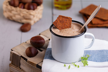 Chestnut soup in white enamel mug with roasted chestnuts 
