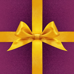 Shiny golden satin ribbon bow on purple background