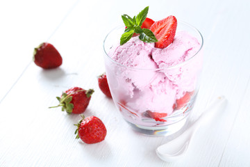 Ice cream in glass with strawberries on white wooden background