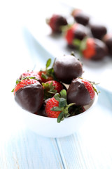 Fresh strawberries dipped in dark chocolate on blue wooden backg