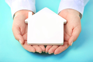 Female hands holding house on turquoise background