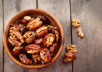 Walnut and date fruit in bowl on wooden table, close-up