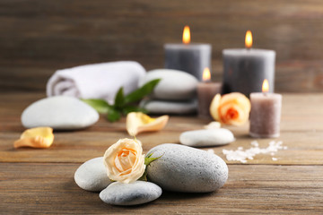 Alight wax grey candles with roses and pebbles on wooden background - relax concept
