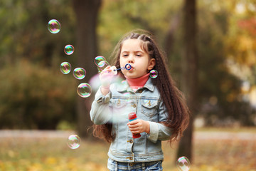 Cute girl blowing soap bubbles in park