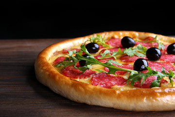 Tasty pizza with salami and olives on wooden table against black background