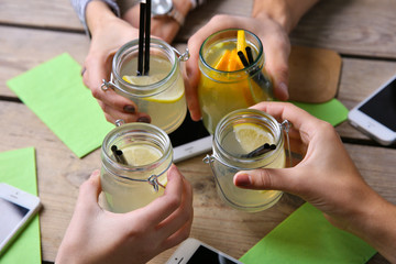 Four hands with smart phones holding cocktails, on wooden table background