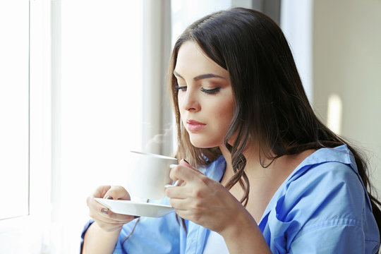 Woman drinking coffee near window in the room