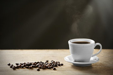 Cup of coffee and coffee grains on wooden table, on gray background