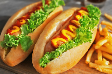 Delicious hot-dogs with French fries on wooden chopping board, close up