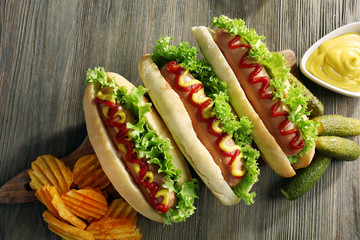 Tasty hot-dogs with chips and pickled cucumbers on wooden background