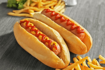 Delicious hot-dog with French fries and vegetables on wooden background