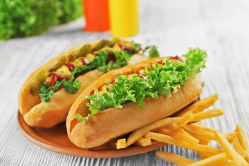 Delicious hot-dog with French fries and vegetables on wooden table