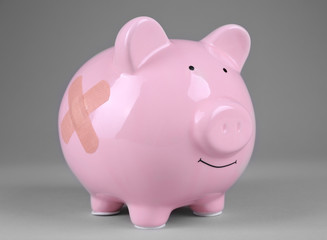 Piggy Bank with adhesive bandage on grey background