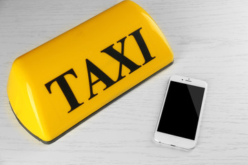 Transportation concept. Yellow taxi sign with smart phone on white wooden background, close up
