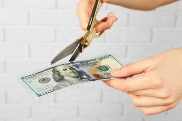 Hands with scissors cutting money on white brick wall background