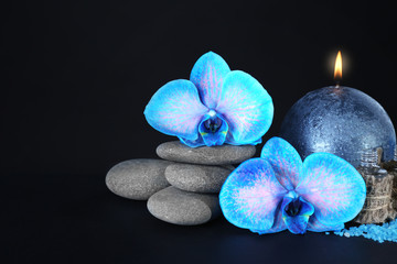Spa set. Beautiful blue orchid with pile of pebbles, candle, sea salt and aroma oil on black background