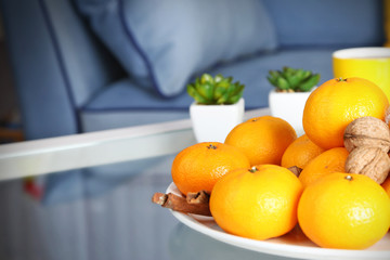 Plate with fresh tangerines on table in living room, close up