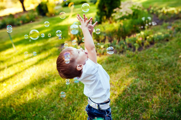 Little boy with soap bubbles in summer park.
