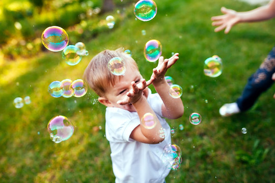 Little boy with soap bubbles in summer park.