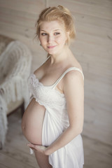 красивая беременная блондинка в светлой комнате. Счастлива