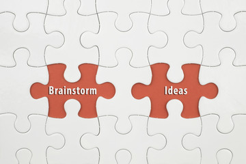 Fototapeta premium Jigsaw puzzle on color paper background with a word Brainstorm and Ideas