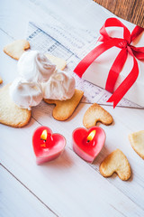 White box with red ribbon, the envelope, meringue, cookies in the shape of heart, red candles. Romantic gift on Valentine's Day on wooden background.