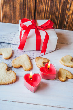 White box with red ribbon, the envelope, meringue, cookies in the shape of heart, red candles. Romantic gift on Valentine's Day on wooden background.