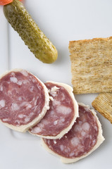 Salami with Pickle and Crackers on a White Plate