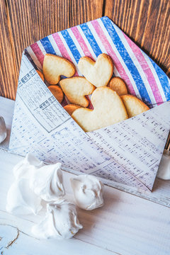 heart-shaped biscuits in romantic envelope and meringue on wooden background.
