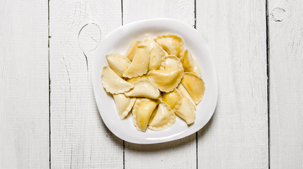 Fresh ravioli with cheese in the plate. On white wooden background.