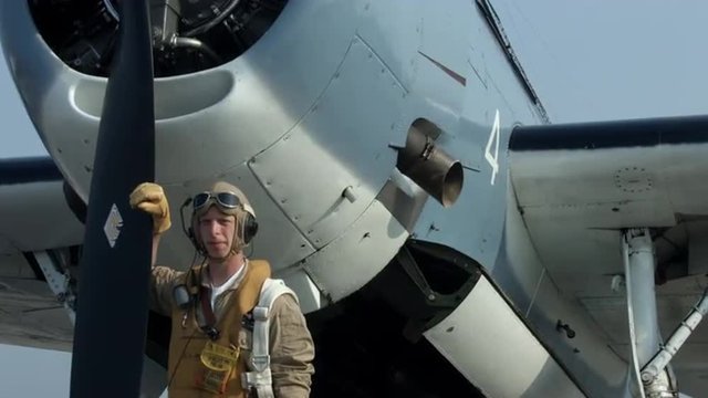 Pilot re-enactor in authentic flight gear standing at the front of a US Navy Grumman Avenger from World War II.  Mute.  Recorded in 4K, ultra high definition.