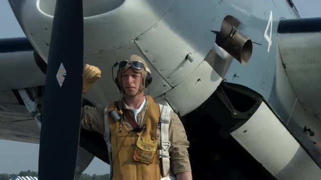 Pilot re-enactor in authentic flight gear looks upwards while standing at the front of a US Navy Grumman Avenger from World War II.  Mute.  Recorded in 4K, ultra high definition.