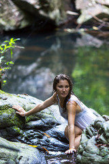 Young beautiful woman on the rocks near the waterfall.