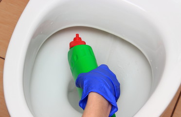 Hand of woman in blue glove cleaning toilet bowl
