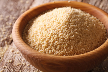 Raw couscous in a wooden bowl on a table close-up. horizontal
