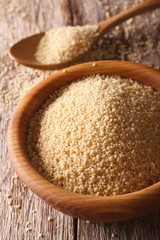 Raw couscous in a wooden bowl and scattered on the table. vertical
