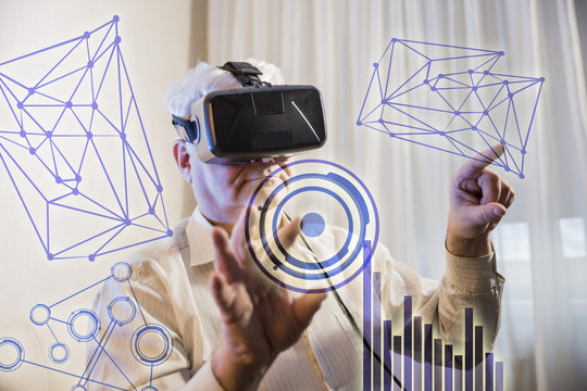 the silver-haired man getting experience using VR-headset glasses of virtual reality presses imaginary interactive monitor on the background of the graphs and charts