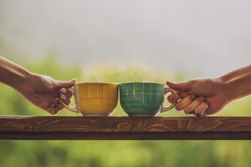 Fototapeten Hands holding mug with hot beverage, with tea on a wooden stand © kuzmichstudio