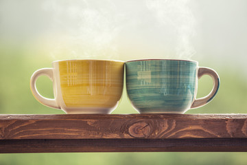 Mugs with a hot drink with tea on a wooden stand outdoors